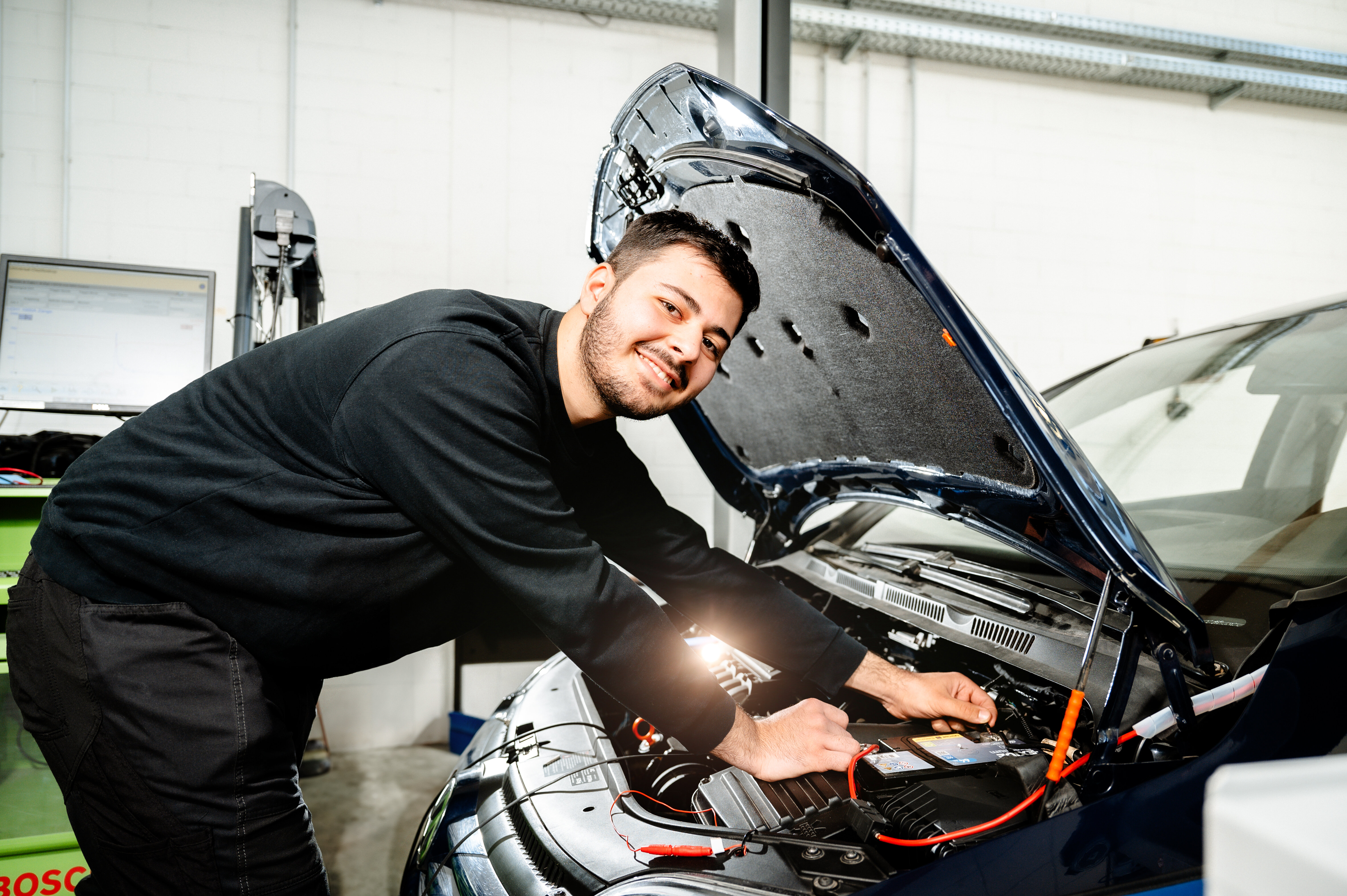 Ein Mechaniker arbeitet an einem Auto, während er Kabel anschließt. Er lächelt und zeigt Engagement in seiner Werkstatt.