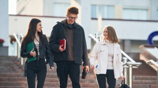 Drei junge Menschen laufen eine Treppe hinunter. Sie tragen Rucksäcke und Schulsachen.