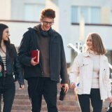 Drei junge Menschen laufen eine Treppe hinunter. Sie tragen Rucksäcke und Schulsachen.