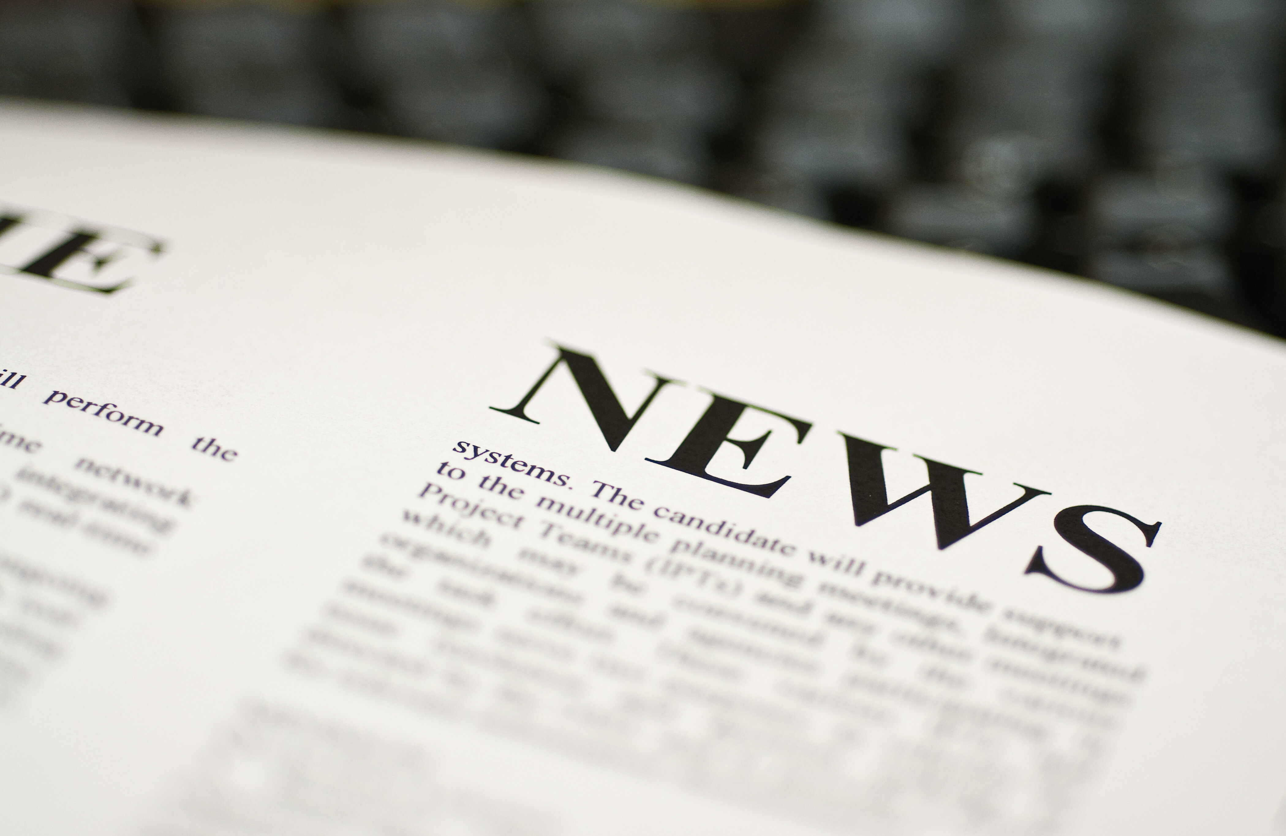 Das Bild zeigt eine Nahaufnahme eines Textes mit dem Wort "NEWS" in großer Schrift, umgeben von weiteren Textdetails auf Papier.