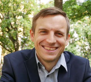 Das Bild zeigt Josip Primporac, einen Mann in einem blauen Sakko, umgeben von grünen Bäumen. Er wirkt freundlich und entspannt.