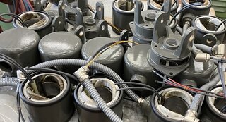 Das Bild zeigt eine Ansammlung von grauen mechanischen Komponenten, wahrscheinlich Teile von Maschinen oder Geräten, mit Kabeln und Anschlüssen.