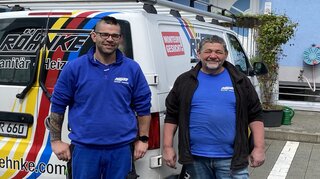 Das Bild zeigt zwei Männer in blauen Arbeitsshirts vor einem weißen Lieferwagen mit dem Logo einer Sanitärfirma.