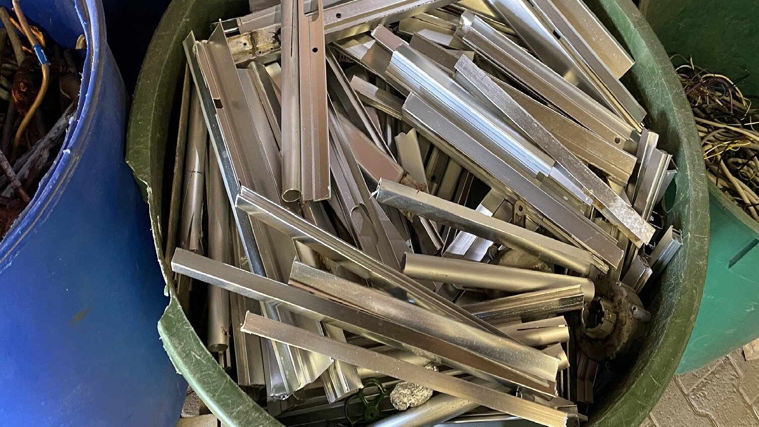 Das Bild zeigt einen Eimer voller Metallteile, darunter zahlreiche Aluminiumprofile. Die Teile sind ungeordnet und teilweise überlappt.