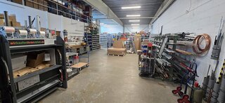 Das Bild zeigt einen großen, gut organisierten Lagerraum mit Regalen voller Materialien, Werkzeugen und Kartons. Alles ist ordentlich angeordnet.