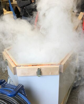 Das Bild zeigt einen dichten Nebel, der aus einer offenen Holzkiste aufsteigt, vermutlich durch einen Rauch- oder Dampferzeuger erzeugt.