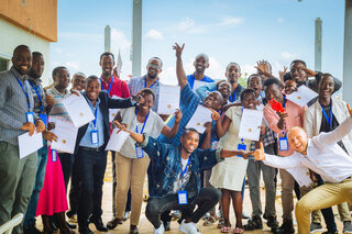 Die Gruppe von Menschen feiert auf einer Terrasse, alle halten ihre Zertifikate hoch. Glückliche Gesichter und eine festliche Stimmung prägen das Bild.