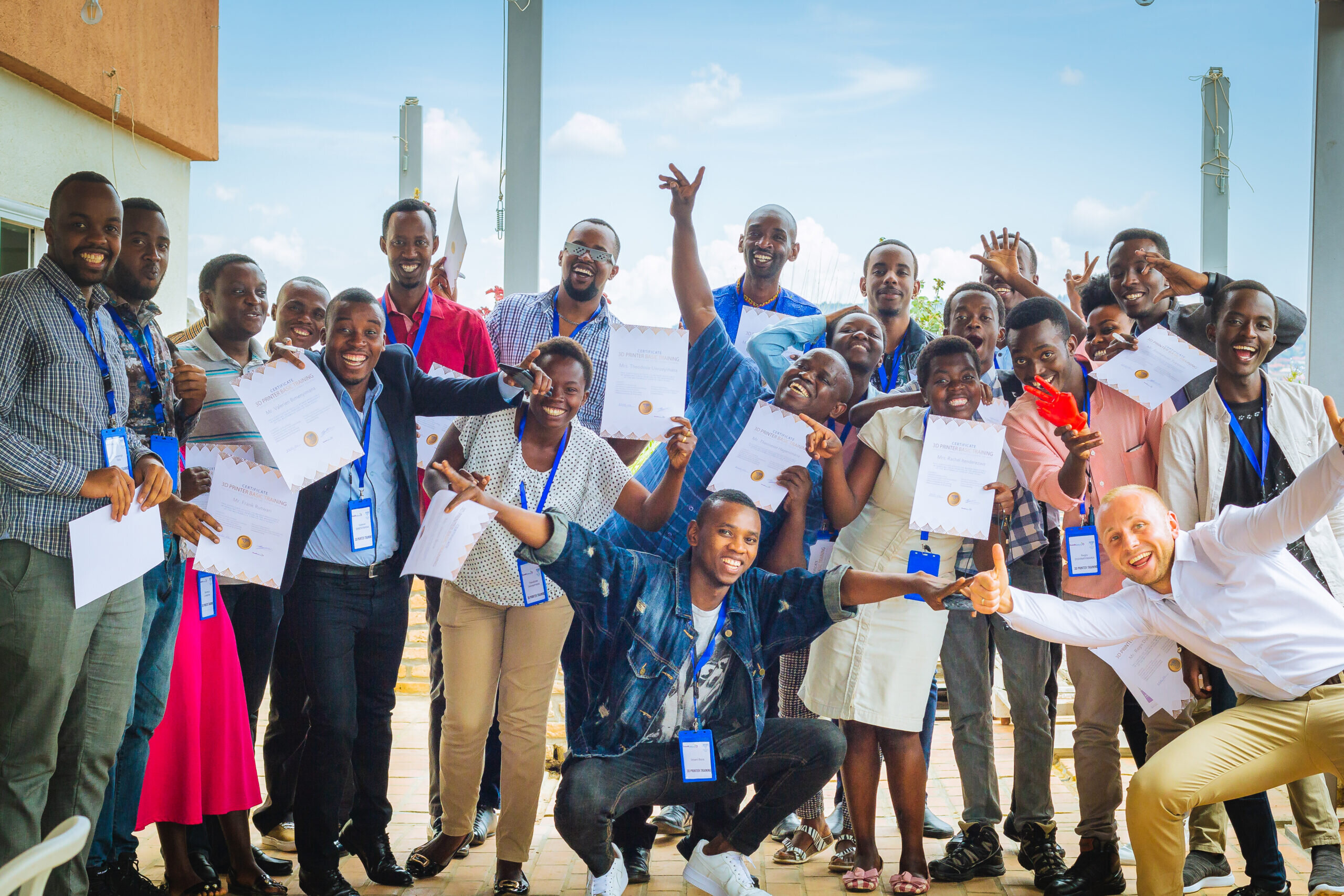Die Gruppe von Menschen feiert auf einer Terrasse, alle halten ihre Zertifikate hoch. Glückliche Gesichter und eine festliche Stimmung prägen das Bild.