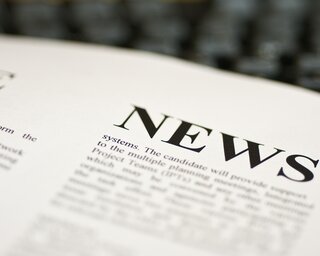 Das Bild zeigt eine Nahaufnahme eines Textes mit dem Wort "NEWS" in großer Schrift, umgeben von weiteren Textdetails auf Papier.