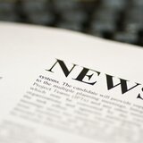 Das Bild zeigt eine Nahaufnahme eines Textes mit dem Wort "NEWS" in großer Schrift, umgeben von weiteren Textdetails auf Papier.