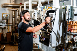 Ein junger Mann arbeitet an Maschinen in einem technischen Umfeld. Er überprüft Geräte und sorgt für reibungslose Abläufe.